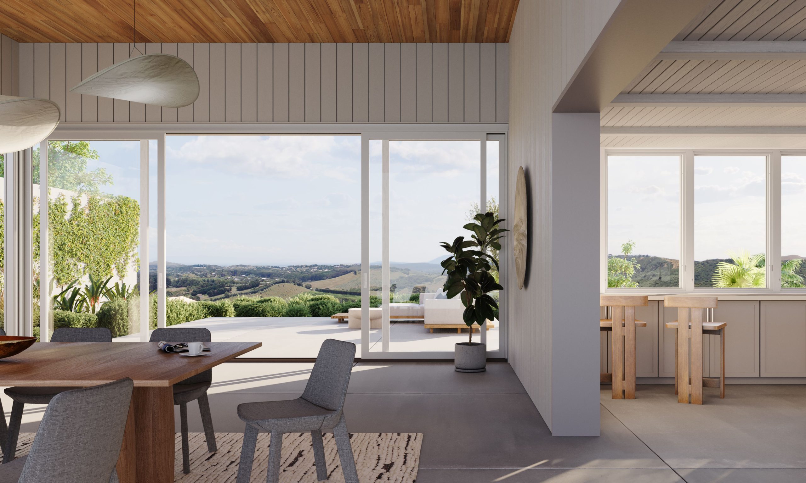 Modern dining and kitchen area with large windows and sliding glass doors opening to a patio and scenic hills in the background; natural light fills the space, which features wooden furniture and indoor plants.